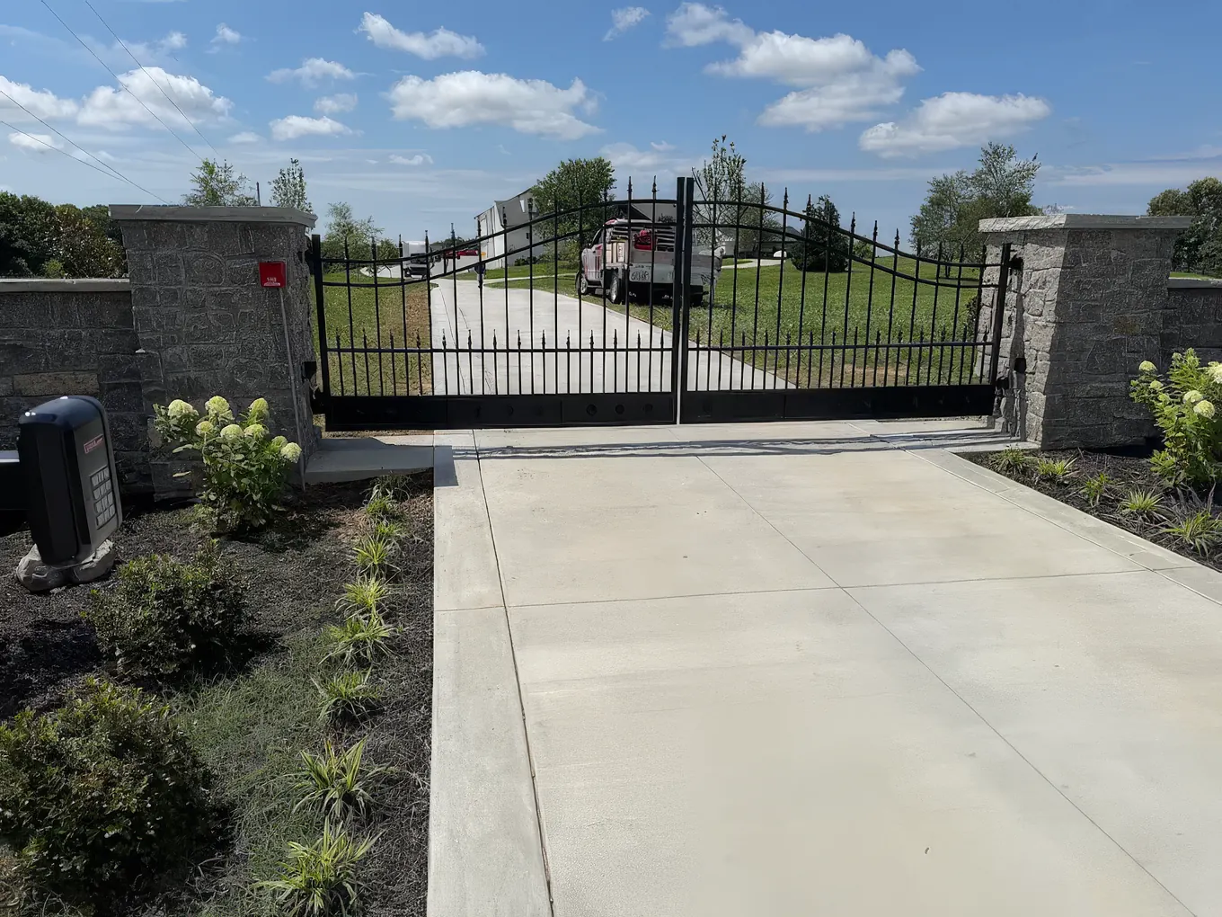 Ornamental spear-top iron driveway gate set between stacked stone columns with keypad